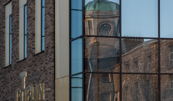 An image of a clock tower reflected in a window and a brass tu dublin logo