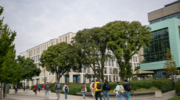 Image for students walking along campus with trees and buildings in the background