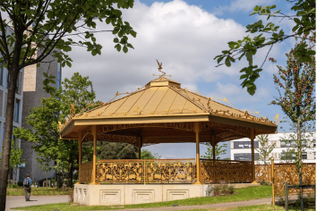 a round bandstand with gold railings and a roof