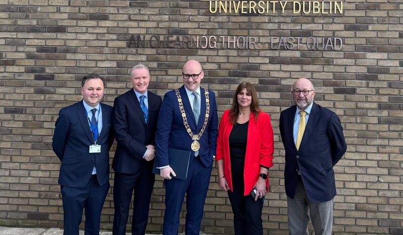 A group of people pose for a photo in front of a bronze tu dublin sign
